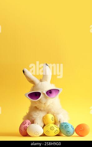 Easter bunny in sunglassis with colorful easter eggs on a yellow background Stock Photo