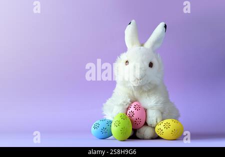 Easter bunny with colorful easter eggs on a violet background. Stock Photo