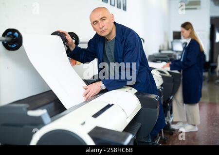 Service man uses plotter and checks functionality in printing shop Stock Photo