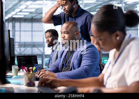 Group of programmers in data center using diagnostic tools and system monitoring software to identify root cause of errors. Colleagues collaborating in server farm, mending equipment together Stock Photo