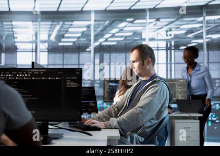 System administrator implements cybersecurity measures to protect data center assets and information. Man in server hub workspace monitoring and analyzing metrics to enhance operational effectiveness Stock Photo