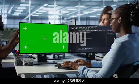 IT technician looking at green screen PC, working in data center, ensuring optimal performance. Employees monitoring energy consumption across server rigs using chroma key monitor, camera B Stock Photo