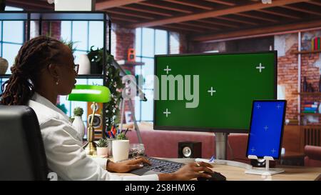 Student at home browsing internet on isolated screen computer and tablet, doing homework. Girl in apartment reading articles on chroma key PC and device for school tasks, camera A Stock Photo