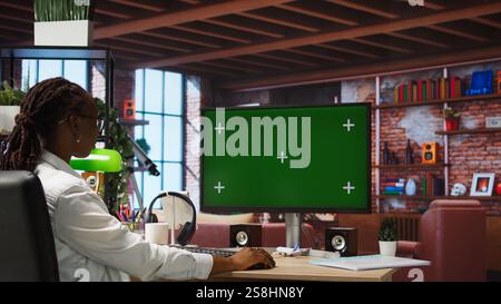 Student at home browsing internet on green screen computer, doing homework, researching information online. Girl in apartment reading articles on mockup PC for school tasks, camera A Stock Photo