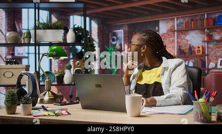 Remote employee pausing work done on laptop at home to pensive thinking. Teleworker in apartment feeling bored by repetitive tasks, stopping work on notebook to daydream, camera A Stock Photo