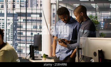 Technician and colleague using device for managing cloud computing platforms training machine learning models. IT staff members in office monitoring company systems using tablet, camera A Stock Photo