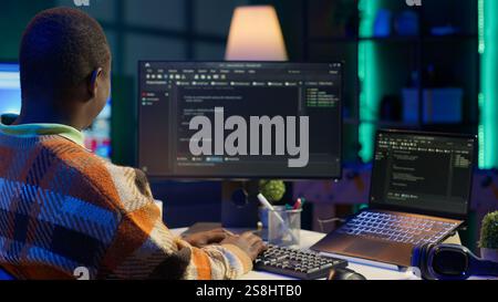 Black software engineer writes complex binary code scripts on computer, cybersecurity. Teleworking IT specialist in home office using programming language to safeguard consumer data. Camera A. Stock Photo