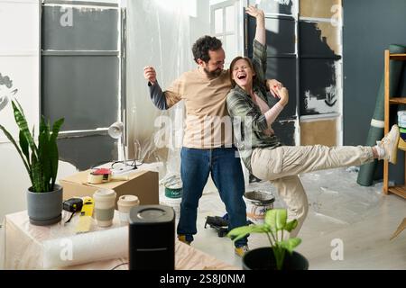 Young excited couple in casual apparel holding by hands and dancing at break during renovation of domestic room Stock Photo