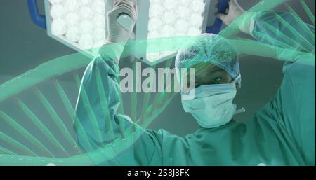 Image of dna strand rotating over african american female surgeon working in theatre Stock Photo