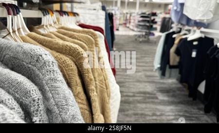 cozy knitted sweaters in shades of gray, beige, and red hanging on a clothing rack in a retail store Stock Photo