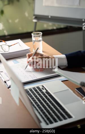 Senior analyst reviewing financial reports and making notes in a modern office setting Stock Photo