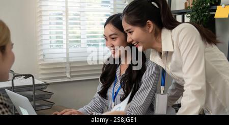 Two smiling businesswomen collaborating over a laptop while discussing a project in a modern office Stock Photo