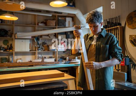 Craftsman inspects table legs and base, ensuring even surfaces and quality construction in workshop Stock Photo