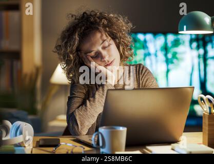 Woman working late at night in her home office, she fell asleep in front of the laptop: burnout, deadlines and insomnia concept Stock Photo