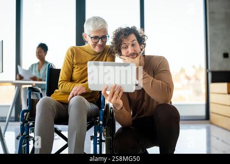 Disabled woman in wheelchair looking at computer, discussing startup project with interracial team Stock Photo