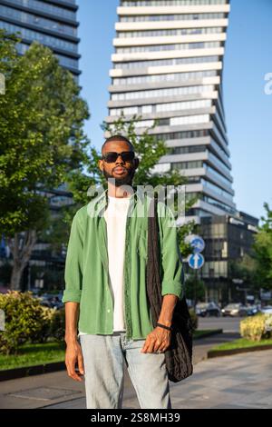 Confident african american man in sunglasses focused looks standing in city skyscraper background. Stock Photo