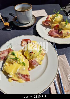 Eggs Benedict with ham, topped with hollandaize sauce and served with coffee at a brunch, outside seating, sunlight table, breakfast, top view Stock Photo