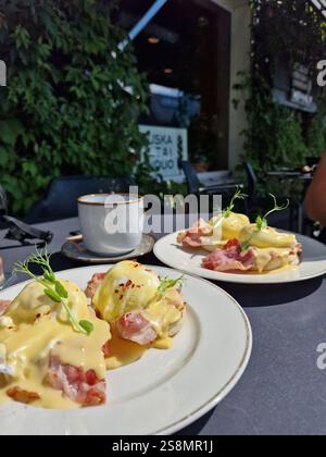 Eggs Benedict with ham, topped with hollandaize sauce and served with coffee at a brunch, outside seating, sunlight table, breakfast, top view Stock Photo