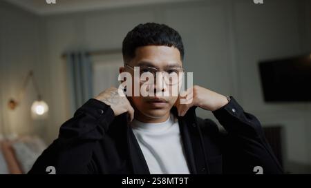 A man in a black jacket and white shirt is adjusting his glasses. Concept of focus and determination as the man prepares himself for the day ahead Stock Photo