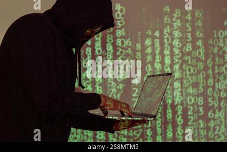 Side view on hacker in black hoody with laptop at binary code digital background. Be aware of hacker attack. Stock Photo
