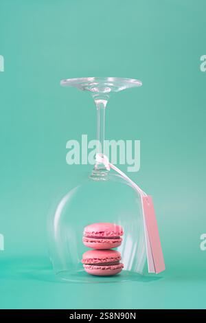 Pink French macarons in a wine glass minimal pastel festive arrangement on turquoise background Stock Photo