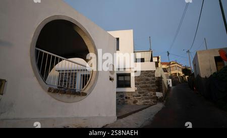 A modern white Mediterranean-style house with a distinctive circular opening in the facade. The clean architectural lines contrast with the rustic hil Stock Photo