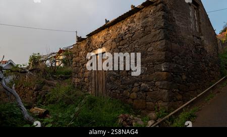 An old stone house with a wooden door, located on a hillside with overgrown vegetation. The rustic structure showcases traditional masonry and a weath Stock Photo