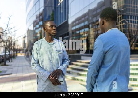 Two senegalese businessmen in traditional dashiki attire are having a conversation outside a modern office building Stock Photo