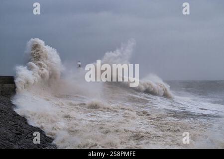 A huge winter storm hitting the coast of the UK. Giant waves crash into a breakwater, with a lighthouse. The sky is grey and moody Stock Photo