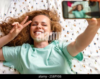 Young woman taking selfie at home while lying on bed Stock Photo