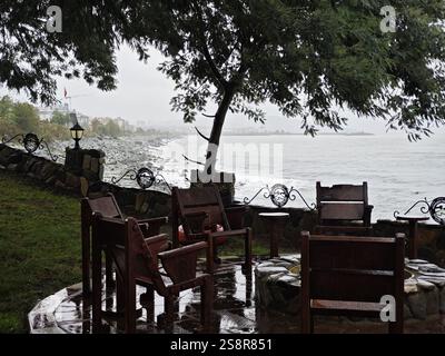 Ardeşen, Rize, Turkey - November 19, 2024: Wooden chairs circle around a stone fire pit in an outdoor seating area by the Black Sea in Turkey Stock Photo