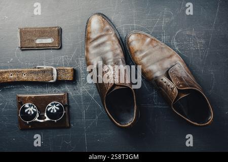 Brown leather shoes with sunglasses, belt, and wallet on a scratched dark surface Stock Photo