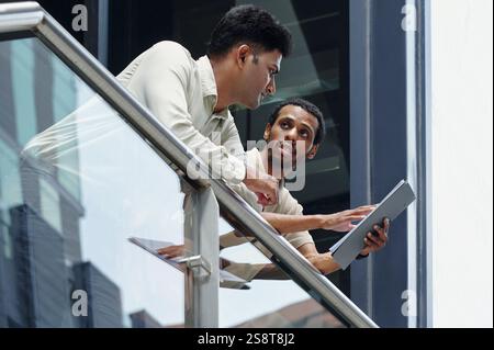 Colleagues standing on balcony of modern office building and discussing business plan together Stock Photo
