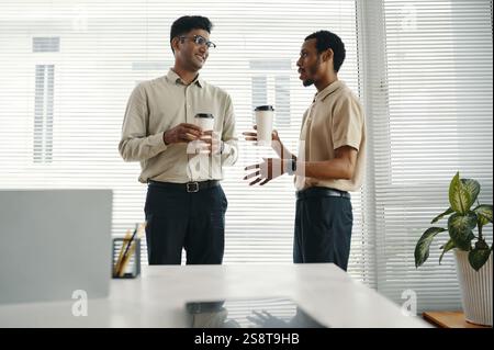 Colleagues with coffee drinks having conversation in office during coffee break Stock Photo