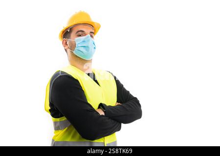 Portrait of male builder in work clothing holding arms crossed wearing protective covid medical surgical disposable mask with blank copyspace isolated Stock Photo