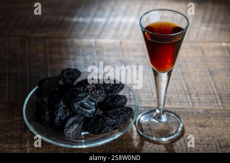 Homemade dark damson plum brandy in glasses on a wooden table, close up. Drink from dry plums Stock Photo
