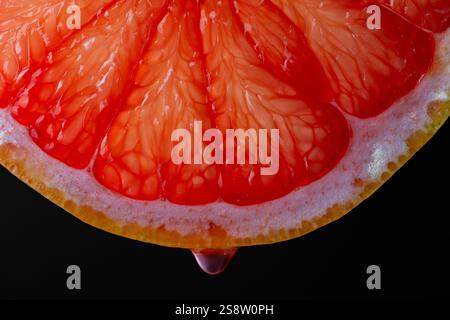 Slice of red grapefruit with juice drops on a black background, macro photography. Texture fresh citrus fruit, close up Stock Photo