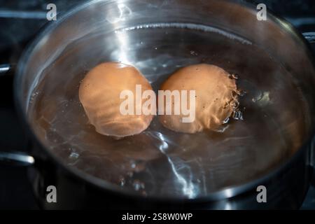 Saucepan with two chicken eggs in boiling water on a gas stove, close up Stock Photo