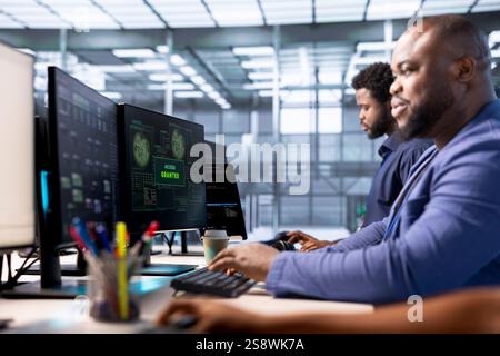 Teamworking technicians in data center getting access granted notification on PC screen, managing to access server files after they were locked by hacker using ransomware, receiving aid from coworkers Stock Photo