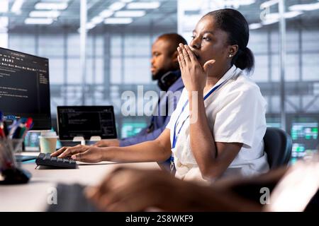 Bored data center technician yawning while creating technical documentation for software applications. Exhausted woman feeling tired after overworking in server hub maintaining databases Stock Photo