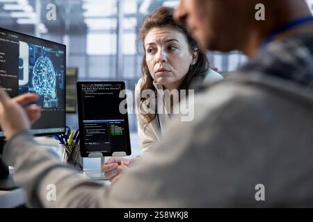 Engineer working with colleague on computer in artificial intelligence data center establishment monitoring hardware energy consumption. Team of AI technicians using PC to check for system failures Stock Photo