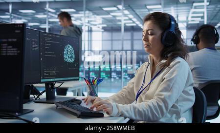 Developer listening music while programming in AI data center used for machine learning training. IT specialist wearing headphones running code to upgrade artificial intelligence tech, camera B Stock Photo