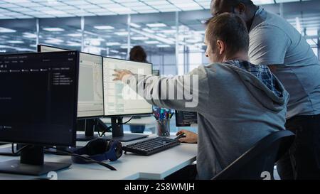Programmer requesting help from manager while working on computer in data center, monitoring hardware energy consumption. Team leader overseeing IT expert checking for system failures, camera B Stock Photo