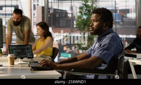 Man with paraplegia conducting code review to fix errors, identifying potential performance and technical issues with software. IT professional with disability in wheelchair optimizing code, camera A Stock Photo