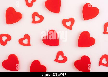 Red wooden hearts scattered on light pink surface in a minimal pattern. Valentines day concept. Texture, background. Stock Photo