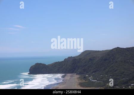 dark green forested hills rising above black sand beach with gentle ocean waves rolling in Stock Photo