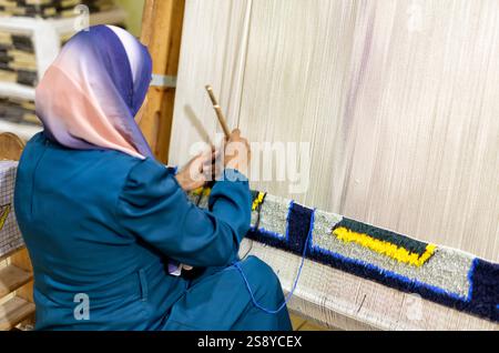 Weaving and production of handmade carpets up close. women's hands weave a carpet. A woman's hand sewing a tapestry. Stock Photo