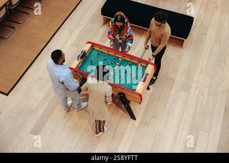 Overhead view of four colleagues gathered around a foosball table in an office. The image highlights teamwork, collaboration, and the balance of work Stock Photo