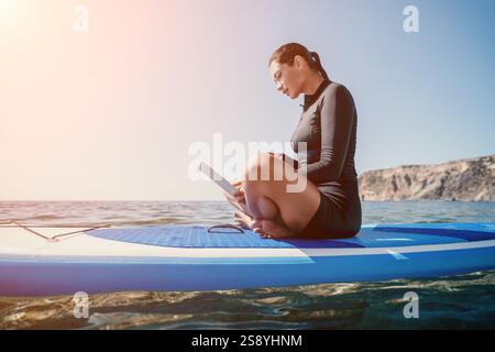 Woman Laptop Paddleboard Working Remotely on Beach Stock Photo