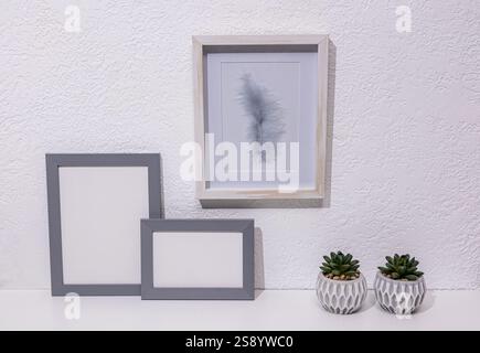 Stylish minimalist decor in light colors on a white table in a modern space. Two gray photo frames, a painting, pots. Front view. eco items Stock Photo